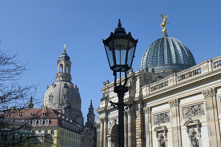 Blick auf die Dresdner Frauenkirche und die Kuppel der Kunstakademie mit goldener Figur, davor eine historische Straßenlaterne.