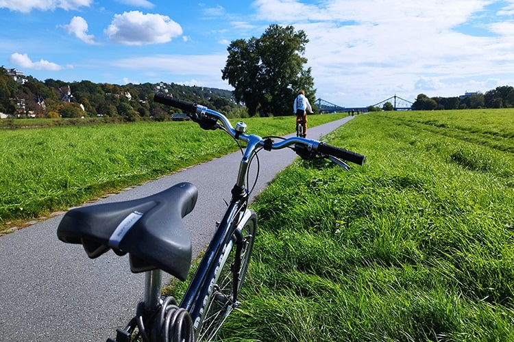 Fahrrad auf einem Elberadweg bei Dresden, im Hintergrund fährt eine Person in Richtung der Brücke 'Blaues Wunder'.