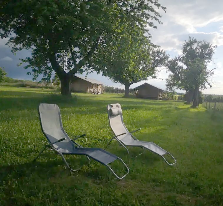 Zeltanhänger auf einer Wiese vor einem langgestreckten Hofgebäude an einem bewölkten Tag